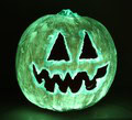 A pumpkin carved with a jagged mouth and triangle eyes glows green in the dark.