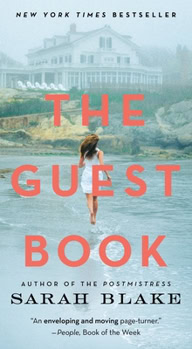 Book cover of The Guest Book by Sarah Blake. The title appears in large coral-red letters over a misty coastal scene featuring a large seaside mansion on a bluff. In the foreground, a woman in a light pink dress stands barefoot at the edge of the water with her back to the viewer. The author's name, Sarah Blake, appears at the bottom, along with the note “Author of The Postmistress.” The cover also includes the text “New York Times Bestseller” at the top.