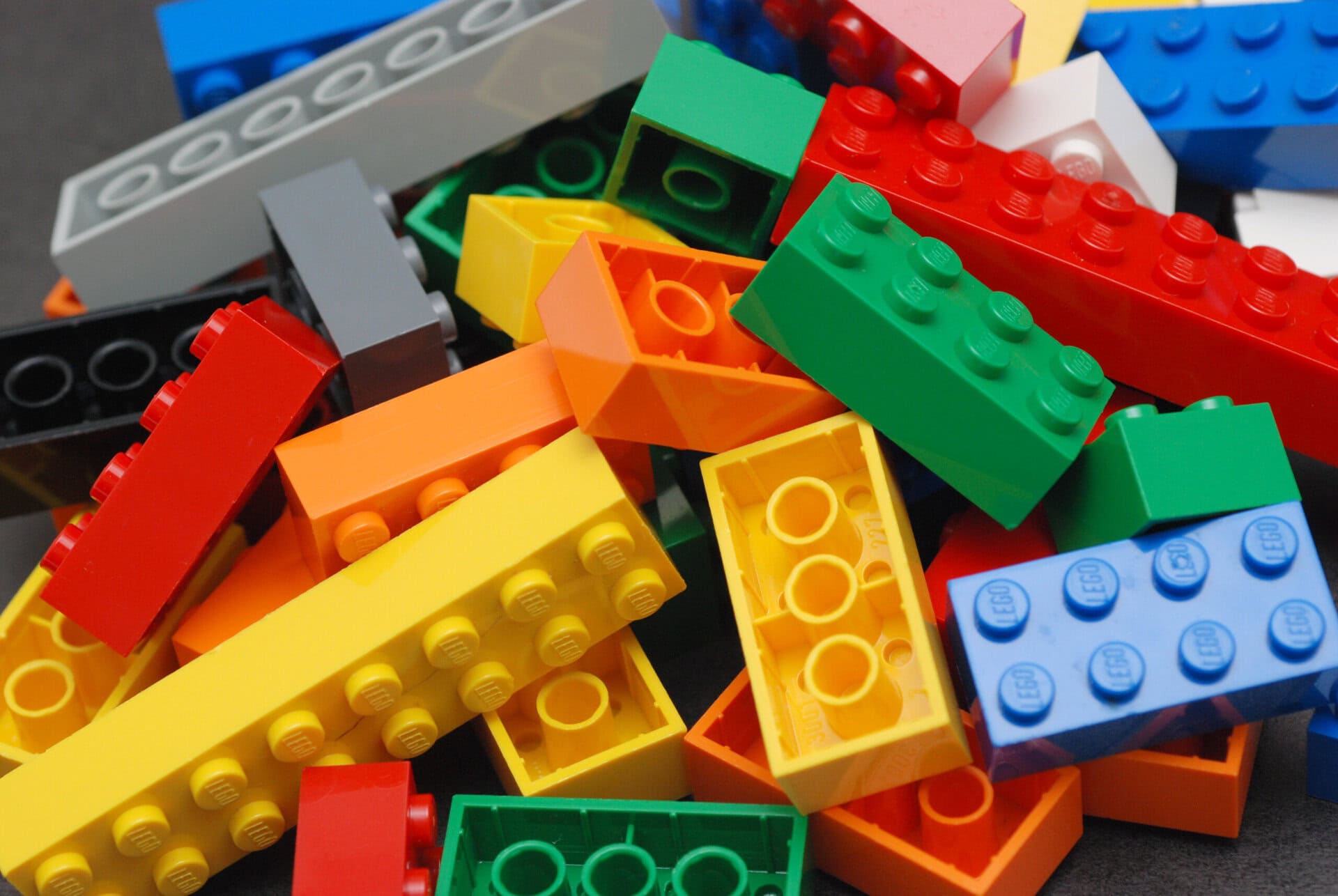 A close-up pile of colorful LEGO bricks in red, yellow, orange, green, blue, gray, and black.