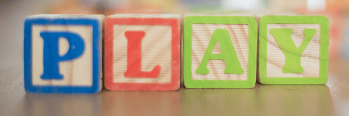Four colorful wooden alphabet blocks spell “PLAY,” with blue, red, and green letters against a softly blurred background.